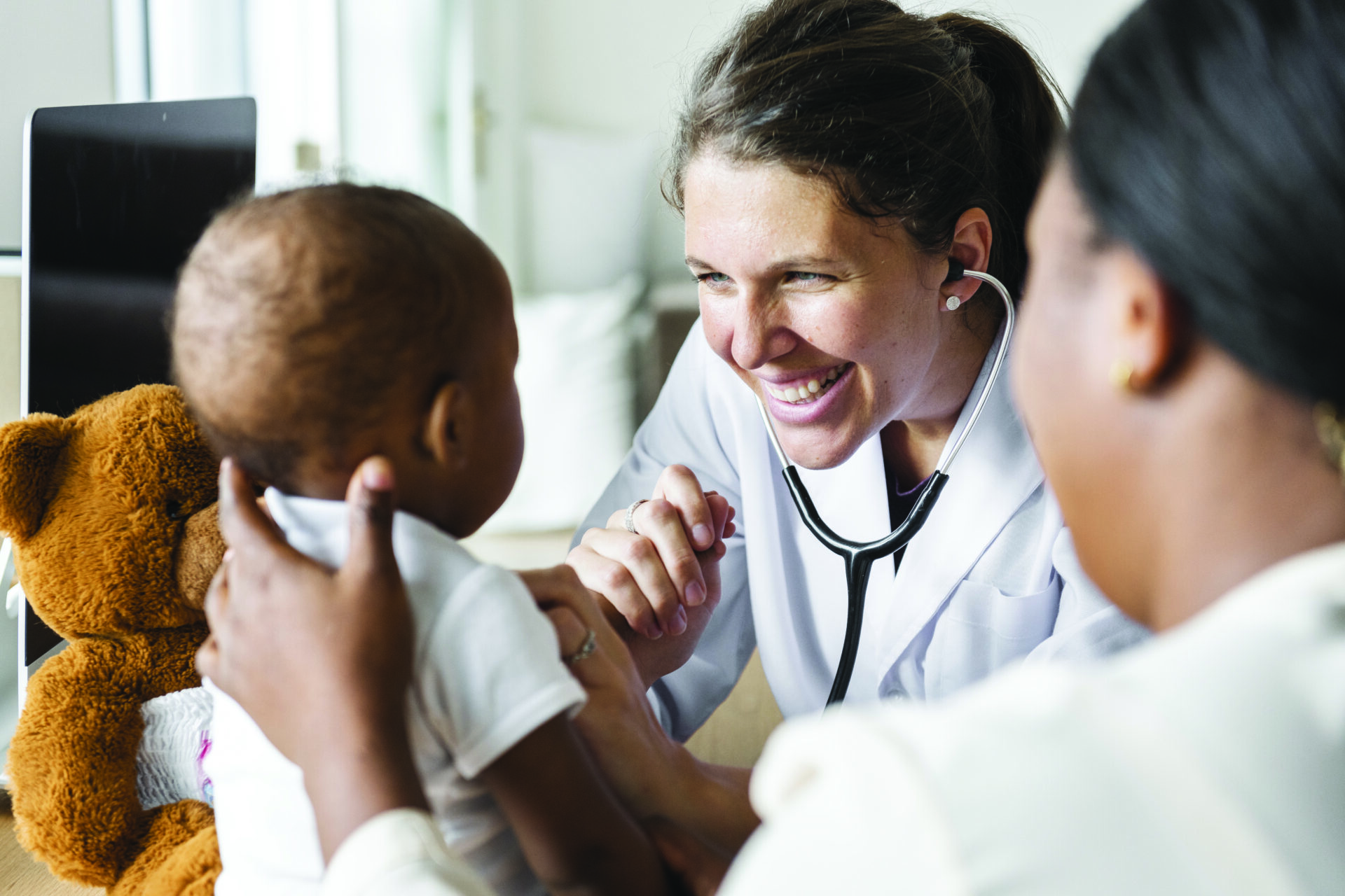 Health professional smiling down at baby being held up by its mother