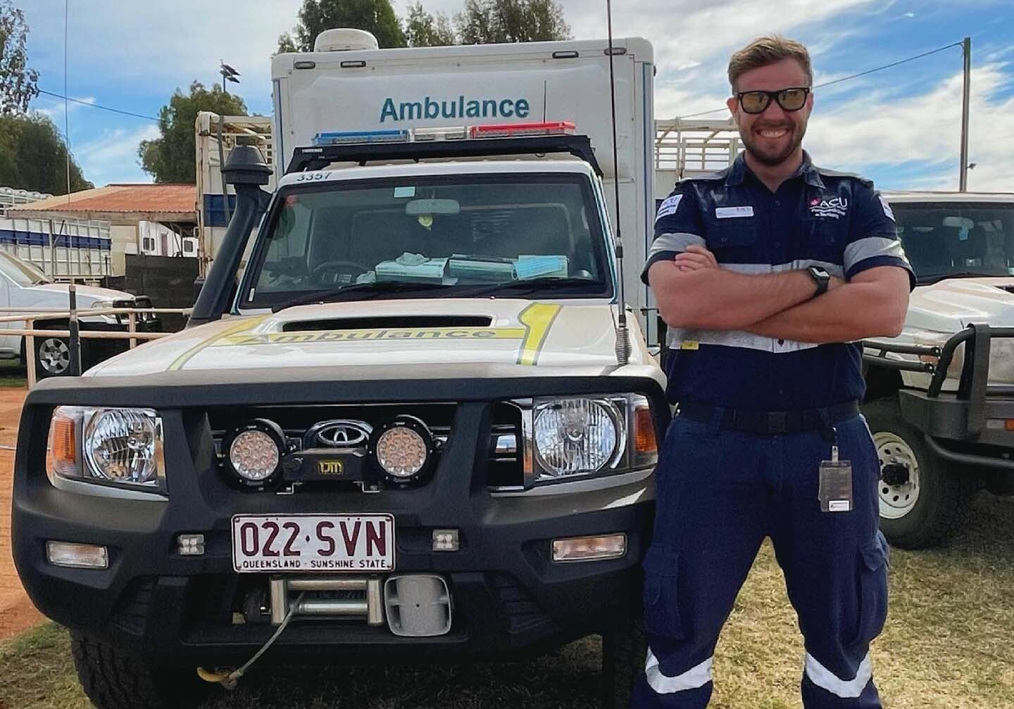 tanford-2 Man standing with arms crossed, smiling, next to ambulance.
