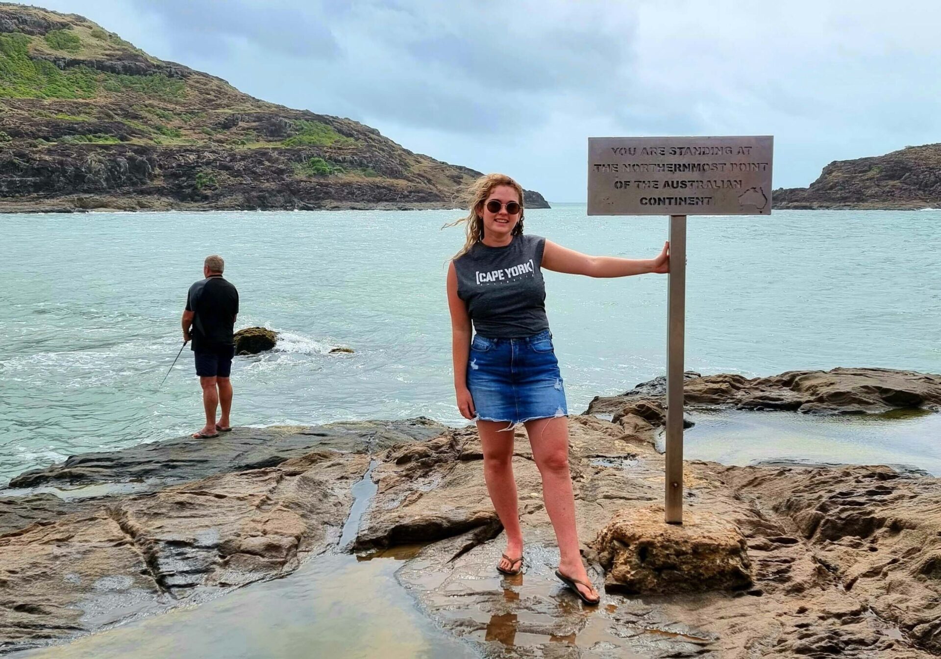 Woman standing holding a sign that reads 'You are standing at the northernmost point of the Australian continent'